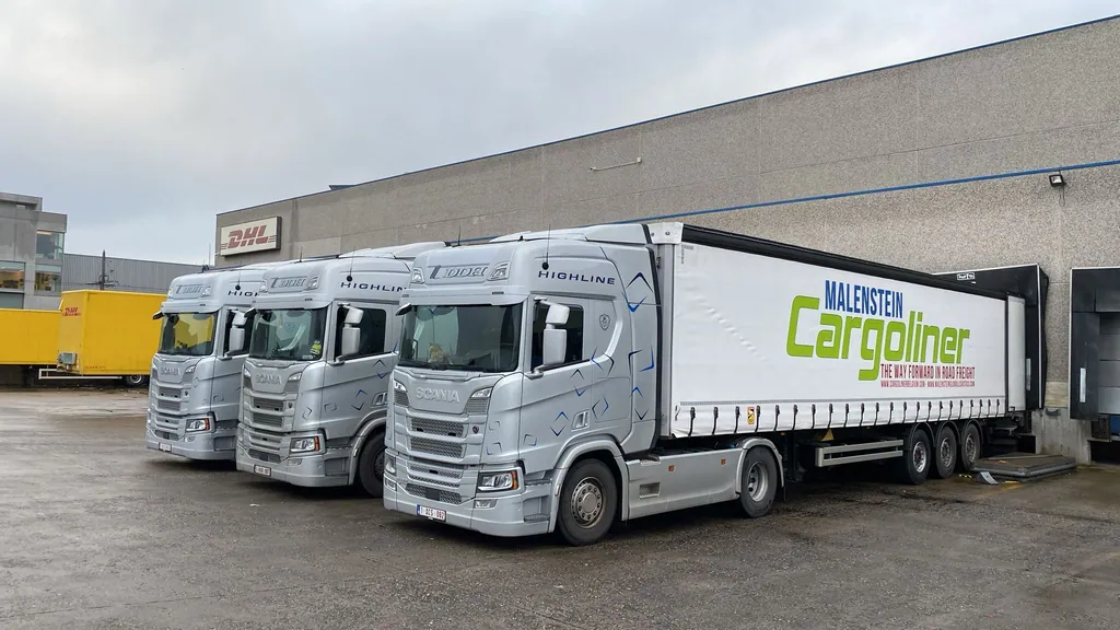 Drie zilverkleurige Scania trekkers met trailers aan een laadkade