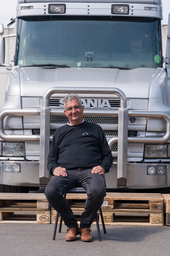 Dirk De Hertogh, de oprichter, zittend op europaletten voor een zilverkleurige Scania