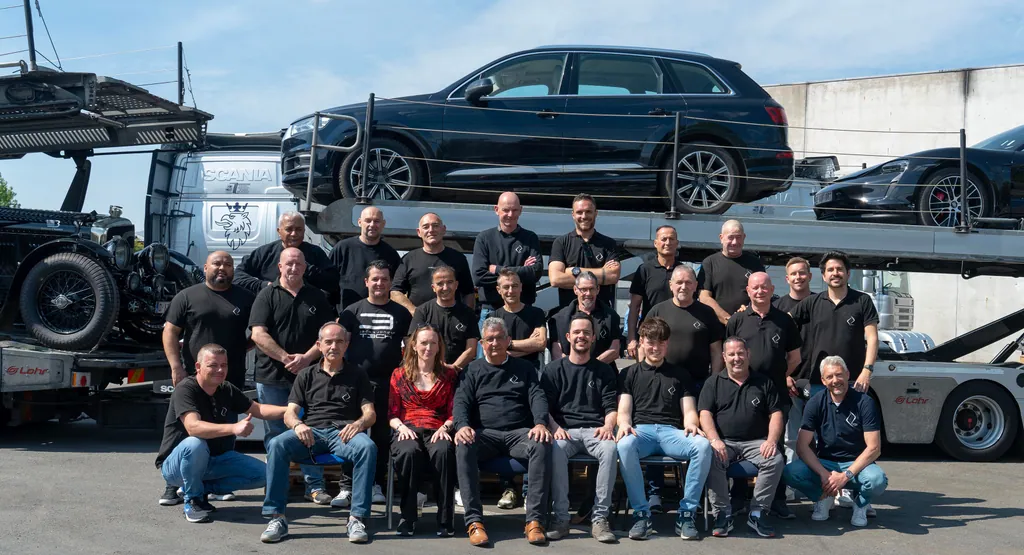 Het team van Transport DDH en El Duque Trans in zwarte poloshirts, met een autotransporter achter hen